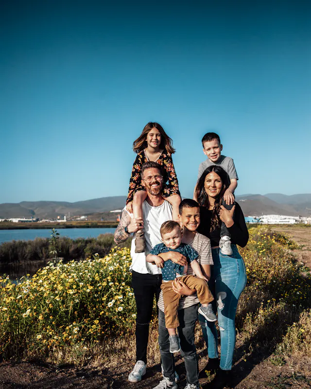 Una familia sonriente al aire libre: los papás cargan a sus hijos frente a un campo de flores amarillas